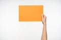 Indoor shot of raised young female`s hand keeping yellow squared paper in parallel to floor, isolated over white background. Hand