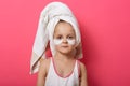 Indoor shot of relaxed little girl has fresh healthy skin, wearing collagen patches under eyes, wears white towel on head and t Royalty Free Stock Photo