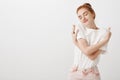 Indoor shot of romantic and sensual european female with ginger hair in stylish outfit, hugging herself gently, smiling