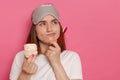 Indoor shot of sad pensive thoughtful woman with blindfold on her forehead, holding marshmallow and toothbrush, looking away, Royalty Free Stock Photo