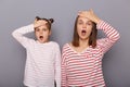 Indoor shot of scared shocked woman and little girl with hair buns wearing casual clothes standing isolated over gray background, Royalty Free Stock Photo