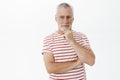 Indoor shot of self-assured wise and intelligent mature retired man with beard and grey hair touching chin with