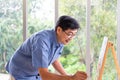 Indoor shot of senior Asian men using brush and oil color to paint on painting canvas. With smile on his face. Happy retirement Royalty Free Stock Photo