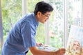 Indoor shot of senior Asian men using brush and oil color to paint on painting canvas. With smile on his face. Happy retirement Royalty Free Stock Photo