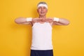 Indoor shot of senior sporty man wearing sleeveless t shirt and headband, keeping hands in front of chest, doing physical