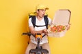 Indoor shot of shocked amazed courier man on bike opens carton pizza box and realize he is mixing up orders, keeps mouth open, Royalty Free Stock Photo