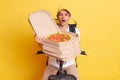 Indoor shot of shocked delivery man holding fresh baked pizza in cardboard box, wearing white t-shirt, sitting on fast motorbike Royalty Free Stock Photo