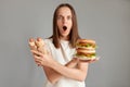 Indoor shot of shocked scared woman looking at camera with big eyes and open mouth, keeps arms crossed, holding sandwich and hot Royalty Free Stock Photo