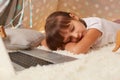 Indoor shot of sleepy little dark haired girl wearing white t shirt or pajama laying on floor in wigwam with closed eyes, falling Royalty Free Stock Photo