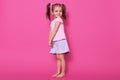 Indoor shot of small child with two pony tails and many colourful scrunchies, glad to be photographed in photo studio, charming Royalty Free Stock Photo