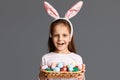 Indoor shot of smiling beautiful little girl wearing bunny ears holding Easter eggs in wicker basket, winning Easter hunt, showing Royalty Free Stock Photo