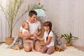 Indoor shot of smiling brunette man wearing white t shirt sitting in wigwam with his daughters and having fun, family playing Royalty Free Stock Photo