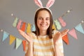 Indoor shot of smiling caucasian woman wearing striped shirt enjoying easter isolated over gray background, raised her arms and