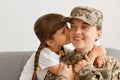 Indoor shot of smiling happy soldier woman wearing camouflage uniform and cap posing with her daughter, mother return home from Royalty Free Stock Photo