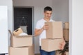 Indoor shot of smiling young adult handsome man posing in a new flat with cardboard boxes, relocating to a new apartment, Royalty Free Stock Photo