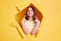 Indoor shot of smiling young adult woman stands in torn paper hole, pointing at her perfect smile and teeth, looking through Royalty Free Stock Photo
