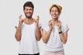 Indoor shot of superstitious Caucasian young woman and man cross fingers, have hope, dream about something pleasant