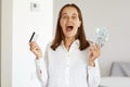 Indoor shot of surprised astonished female wearing white casual style shirt, posing in light room at home, yelling happily,