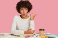 Indoor shot of surprised shocked woman has stupefied facial expression, sits at desk with necessary stationary, drinks