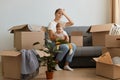 Indoor shot of tired exhausted dark haired woman weairng casual attire sitting on cough with her infant toddler daughter,