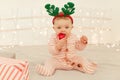 Indoor shot of toddler girl sitting on New year decorations bed and wearing striped long sleeve baby sleeper and festive deer Royalty Free Stock Photo