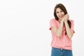 Indoor shot of touched and pleased cute european female model in pink t-shirt, tilting head and holding clenched palms