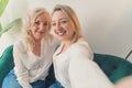 Indoor shot of two related caucasian women in their 40s wearing white elegant shirts takinga selfie, hugging each other Royalty Free Stock Photo