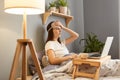 Indoor shot of unhealthy sick woman wearing sleep mask sitting with laptop in bed at home, talking with doctor by video call,