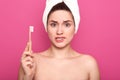 Indoor shot of upset woman biting her lip and holding toothbrush  over pink studio background, posing with bared shoulders Royalty Free Stock Photo