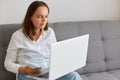 Indoor shot of woman working on portable computer long hours, feels pain in eyes, looking at display of laptop with narrowed eyes