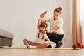 Indoor shot of woman with little girl wearing sportswear doing sport exercises at home, kid sitting on mat on yoga pose and Royalty Free Stock Photo