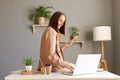Indoor shot of young adult adorable happy businesswoman wearing jacket working on home office and using laptop and mobile phone, Royalty Free Stock Photo
