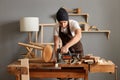 Indoor shot of young adult caucasian carpenter working on woodworking machines in carpentry shop, craftsman sawing wood with an Royalty Free Stock Photo