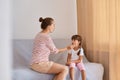 Indoor shot of young adult female speech therapist working with little girl, people wearing casual style clothing, sitting on sofa