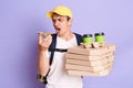 Indoor shot of young adult man courier with thermo backpack, holding mobile phone in hands and screaming, talking to client, Royalty Free Stock Photo