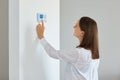 Indoor shot of young adult woman regulating heating temperature with a modern wireless thermostat installed on the white wall at Royalty Free Stock Photo