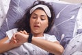 Indoor shot of young attractive woman with dark wavy hair, adorable girl lying in bed with blindfold over forehead and looking at