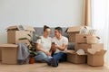 Indoor shot of young couple in love moving in a new apartment, sitting on the floor near, planning to redecorate their new home, Royalty Free Stock Photo