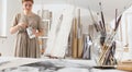 Indoor shot of young female artist in bright white studio while cleaning brushes wearing bohemian chic clothing