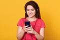 Indoor shot of young girl listening and enjoying music, holding cellular phone in hands and earphones on top of her head, girl Royalty Free Stock Photo