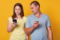 Indoor shot of young marrieds with mobile phones, demonstrates posted photos in social networks, browses in internet. Calm