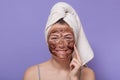 Indoor shot of young smiling attractive woman applying brown cosmetic mask on her face, cleansing her skinat home, usiong Royalty Free Stock Photo