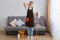 Indoor shot of young woman tired of cleaning house, resting standing near sofa after washing floor with mop, feeling pain in neck Royalty Free Stock Photo