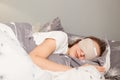 Indoor shot of young woman wearing sleepwear sleeping in a bed with eyes covered with gray mask, lying under blanket, can sleep Royalty Free Stock Photo