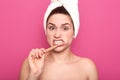 Indoor studio shot of busy unsatisfied young female brushing her teeth with efforts, having unpleasant facial expression, covering