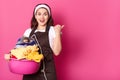 Indoor studio shot of cheerful emotional housewife posing isolated over pink background, holding basin with many clothes and iron Royalty Free Stock Photo