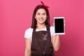 Indoor studio shot of happy attractive energetic female smiling sincerely, holding switched off tablet in one hand, looking