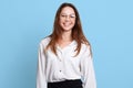 Indoor studio shot of successful cheerful executive standing over light blue background, having positive facial