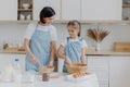 Indoor view of happy mother and daughter prepare tasty supper together, stand next to each other in aprons near kitchen table, Royalty Free Stock Photo