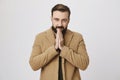 Indoor waist-up portrait of attractive bearded european model in coat, heating hands with warm breath, feeling cold Royalty Free Stock Photo